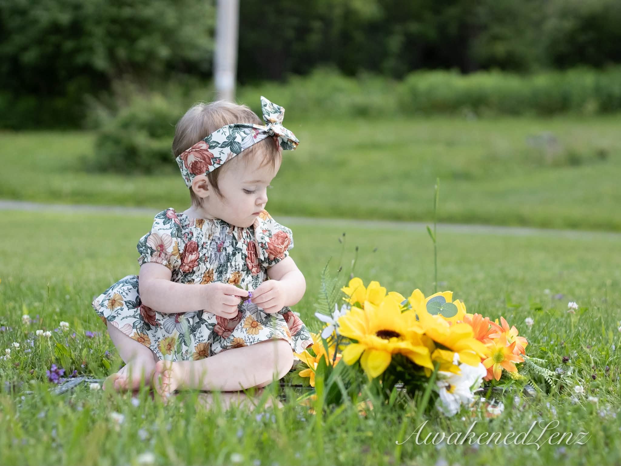 A baby sitting on a mown lawn next to a bundle of cut sunflowers