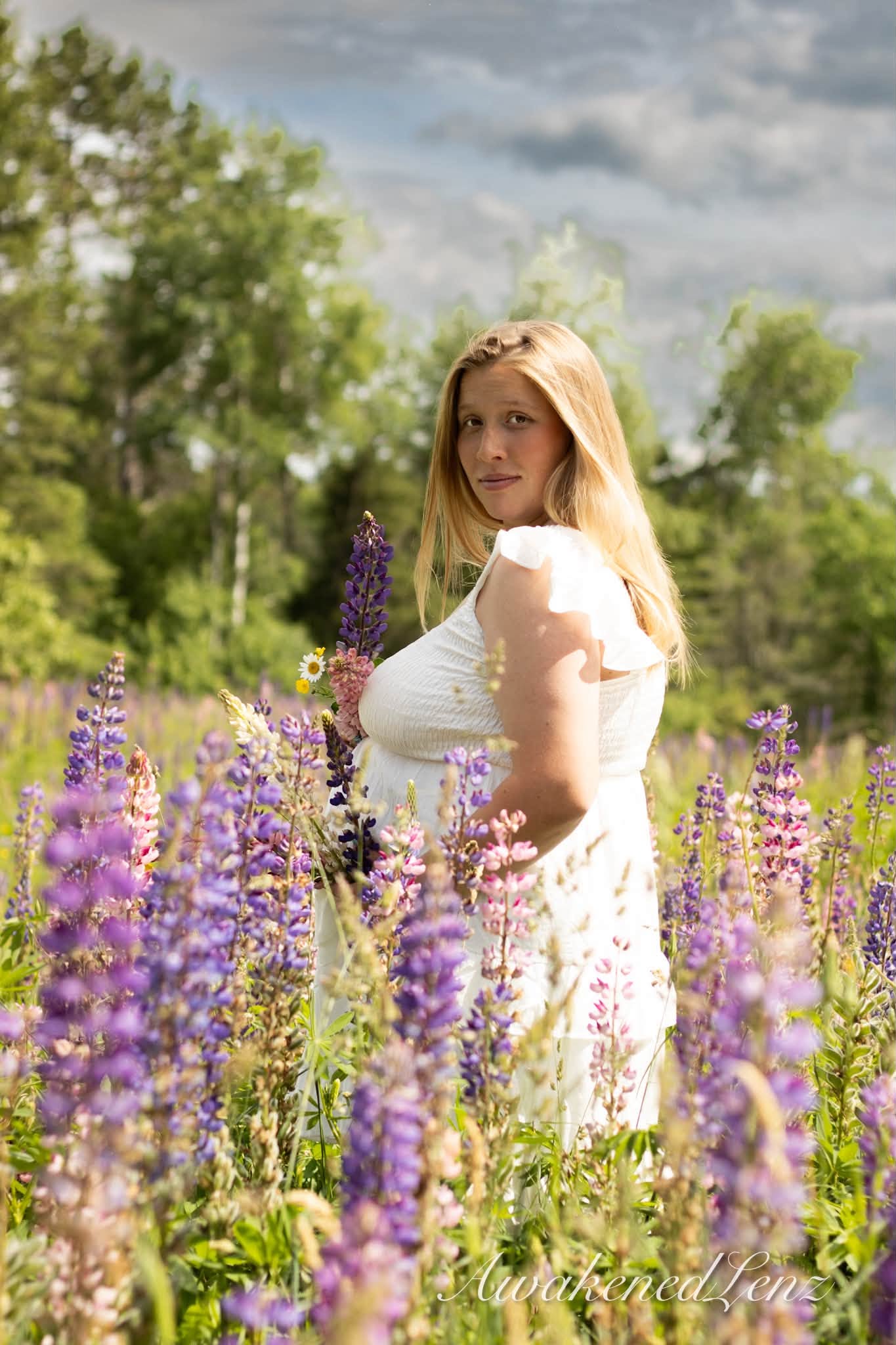 An expecting mother in a long dress standing in a field of lupines