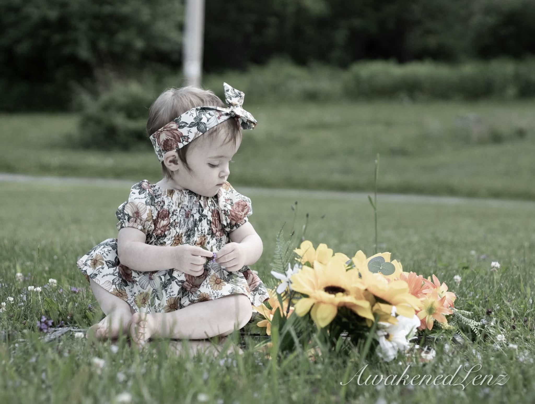 A baby reaching toward sunflowers on the grass, in muted tones