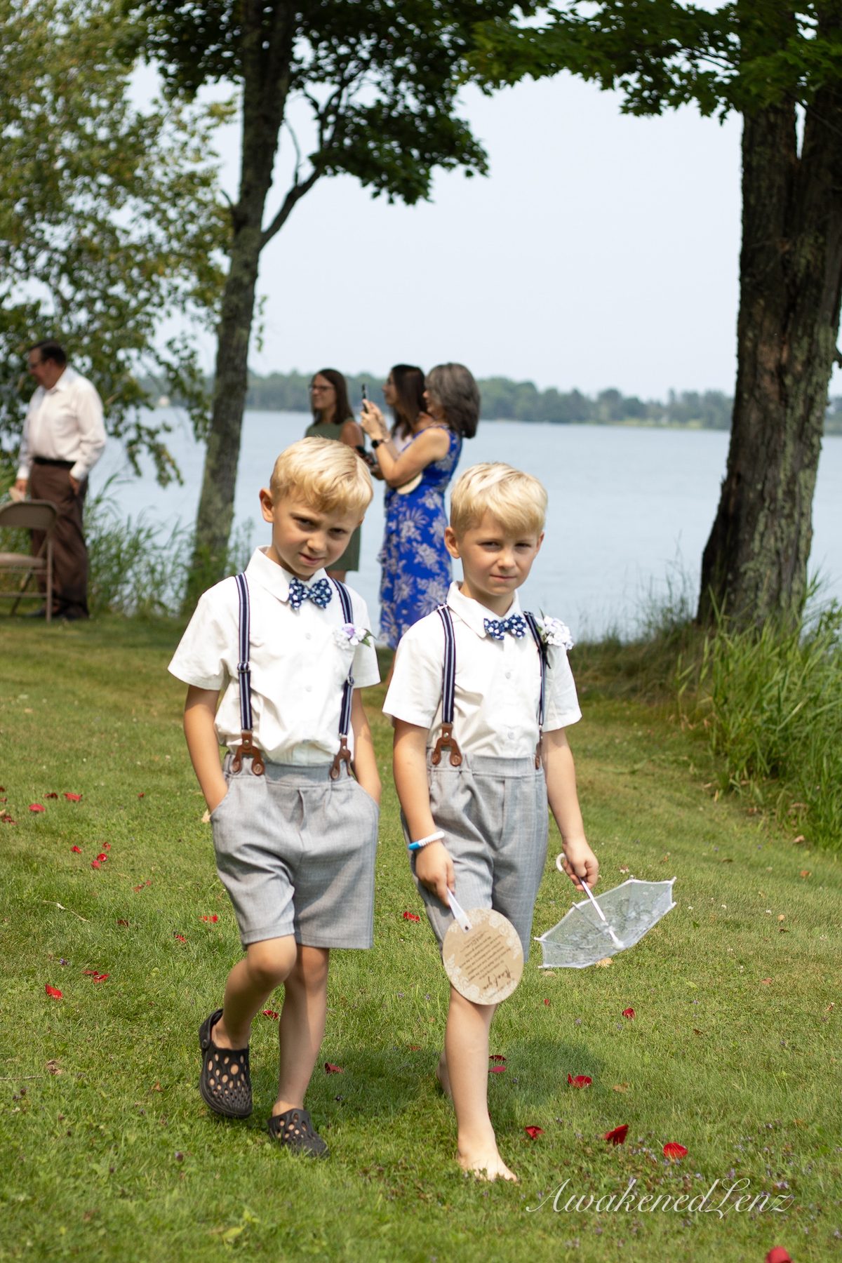 Two boys in suspenders and bow ties walking a petal strewn aisle