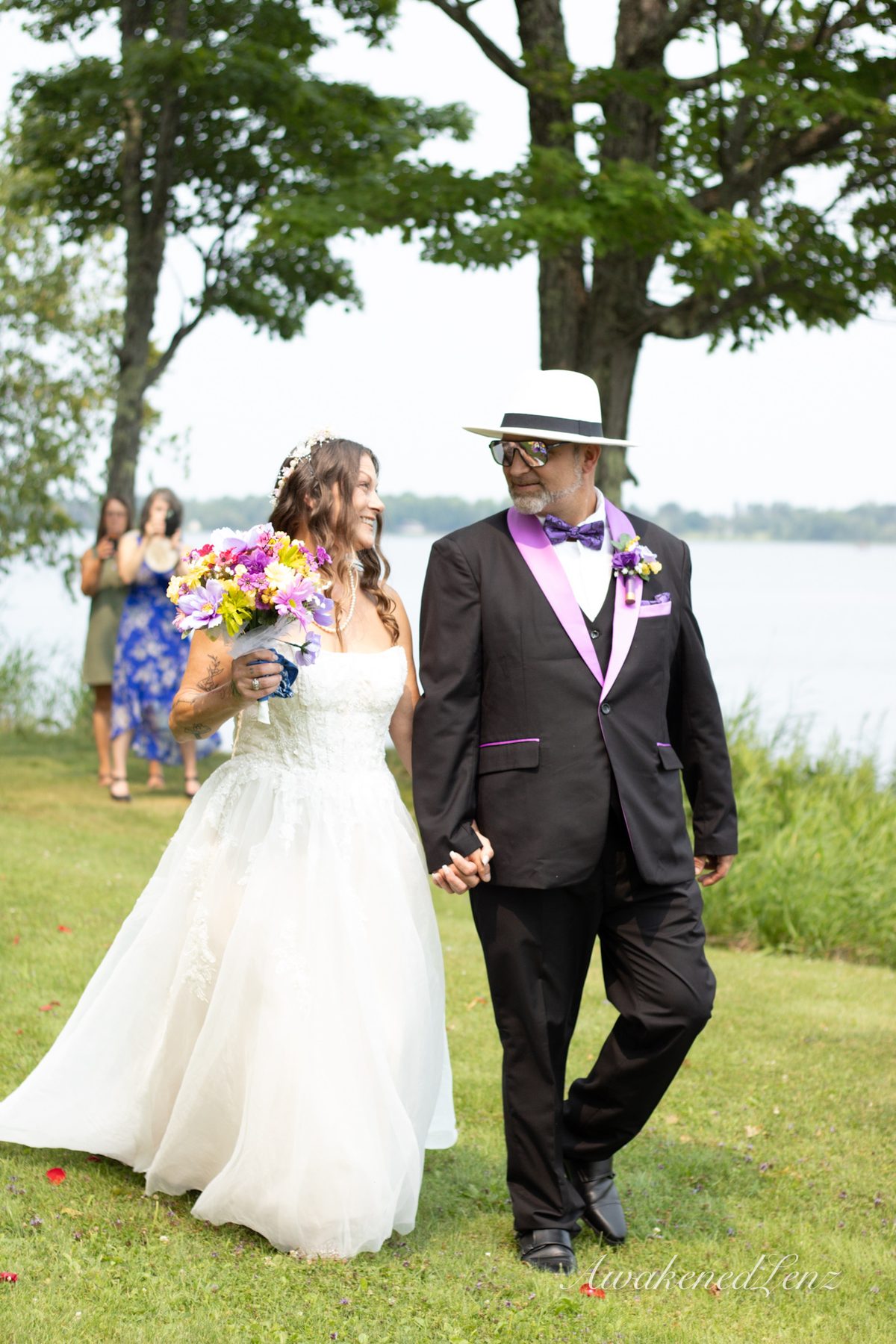 A bride walking down a grass aisle on the arm of an older man in a hat