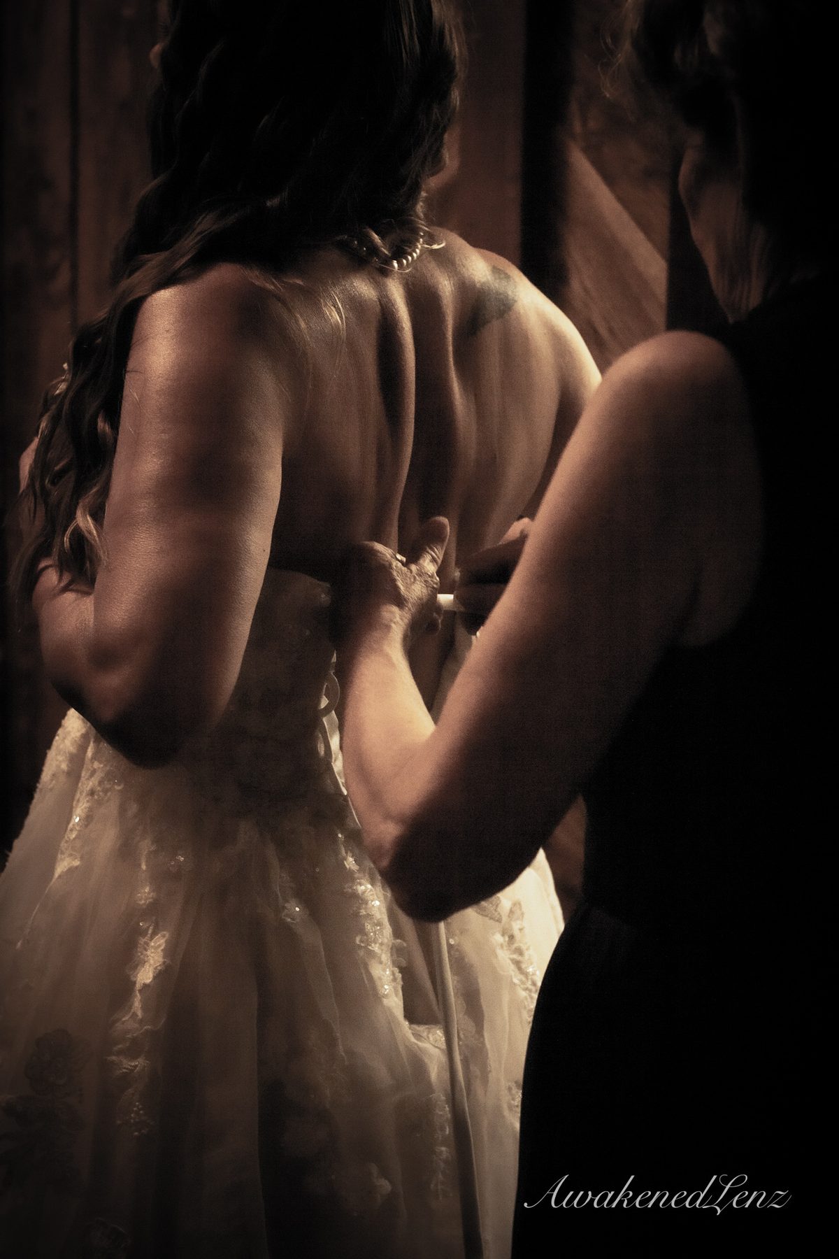 A bride being laced into her gown, lit from one side in warm sepia