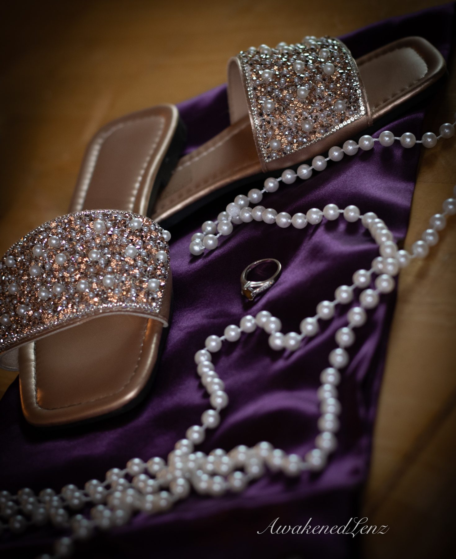 Wedding day details laid out together: sandals, pearls and a ring on purple fabric