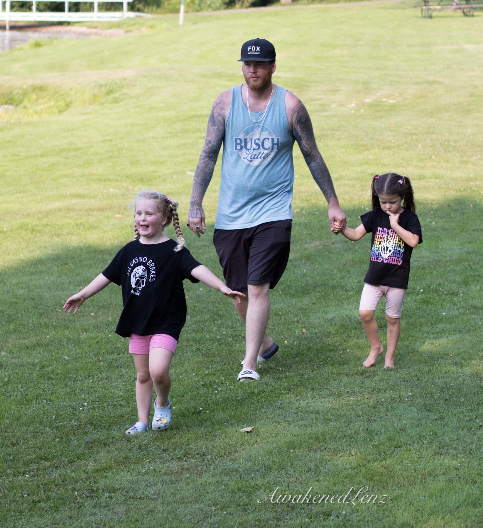 A father and his daughters playing at a park, frame 2 of 2