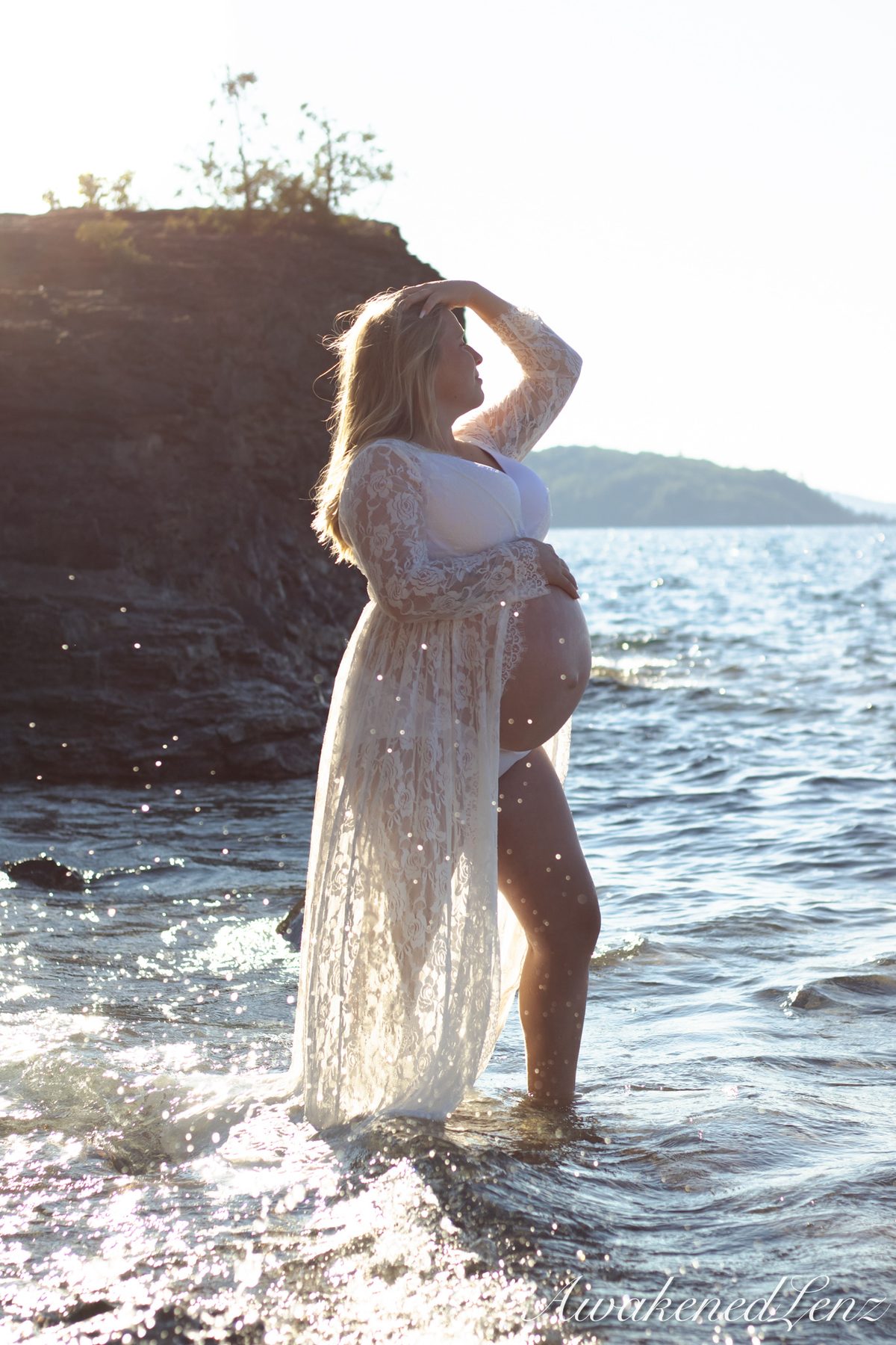 A maternity session on a rocky lakeshore at golden hour, frame 12 of 45