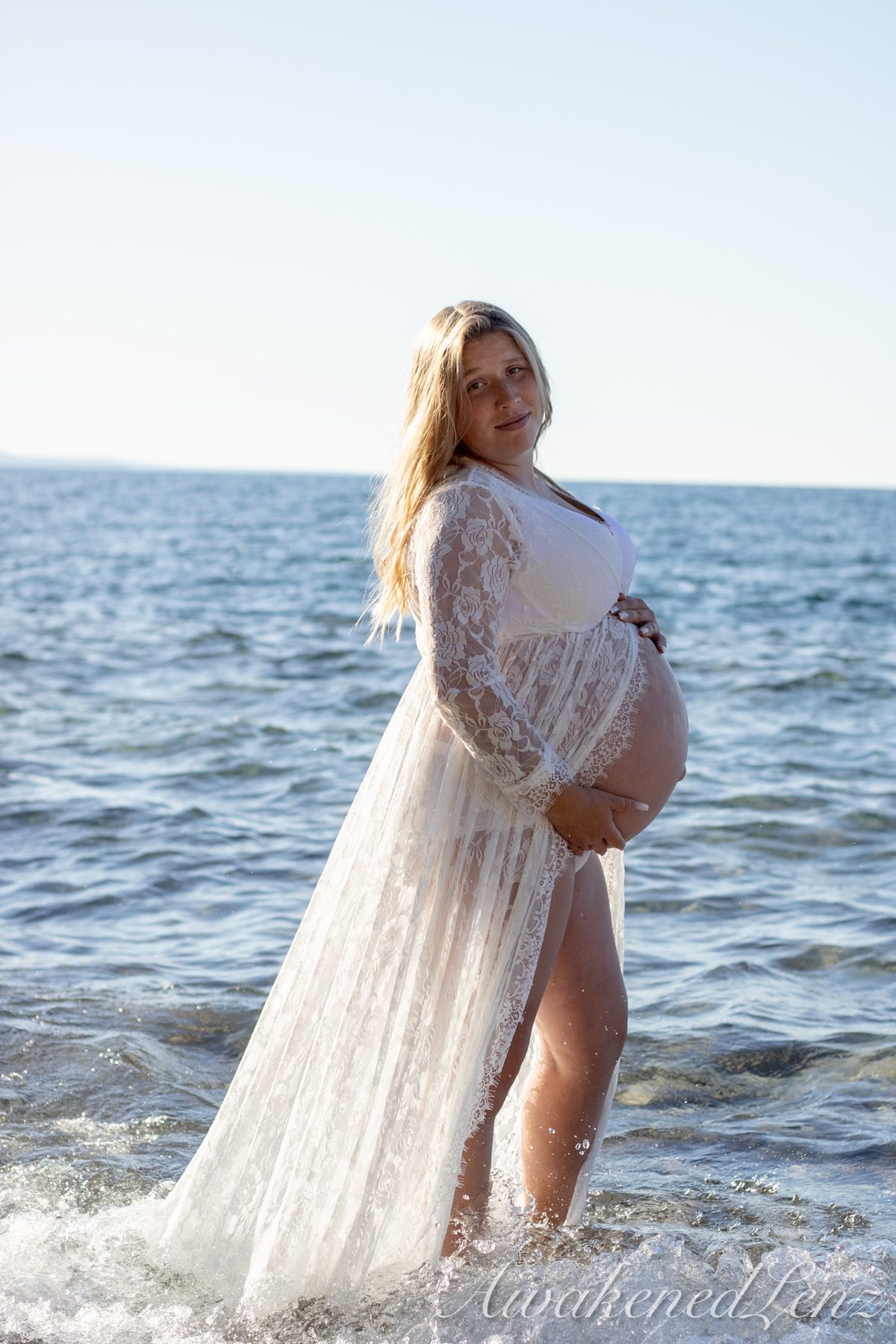 An expecting mother in a lace dress at the water's edge