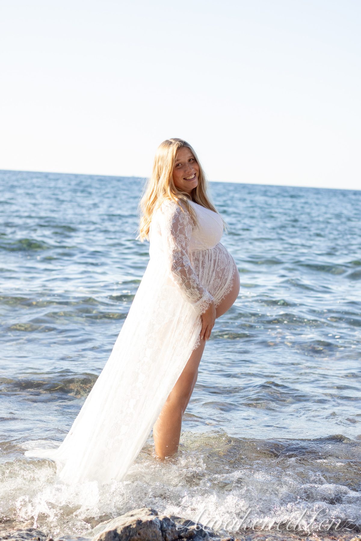 A maternity session on a rocky lakeshore at golden hour, frame 14 of 45