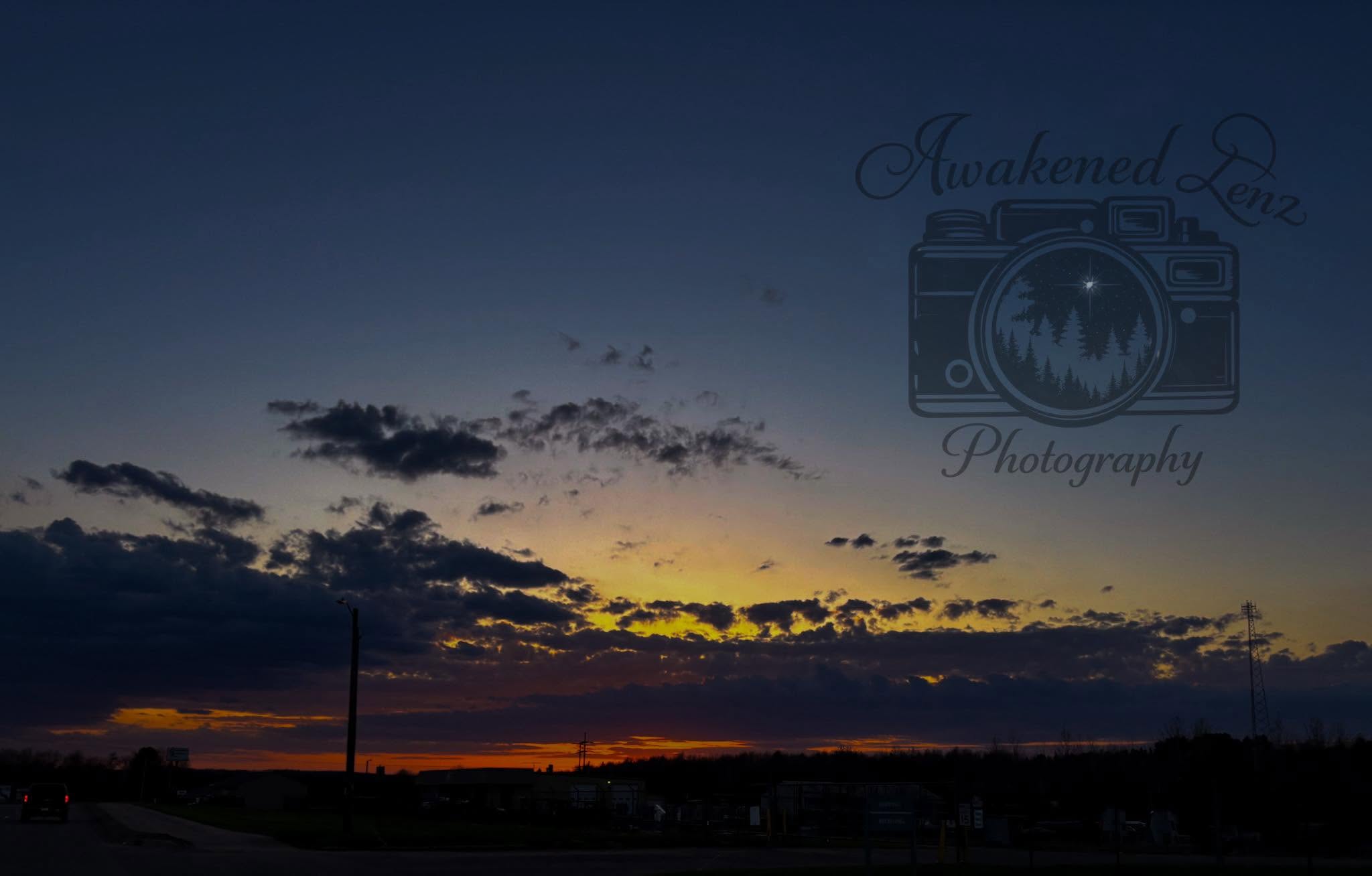 A wide sunset over a small town skyline with a band of gold under dark cloud